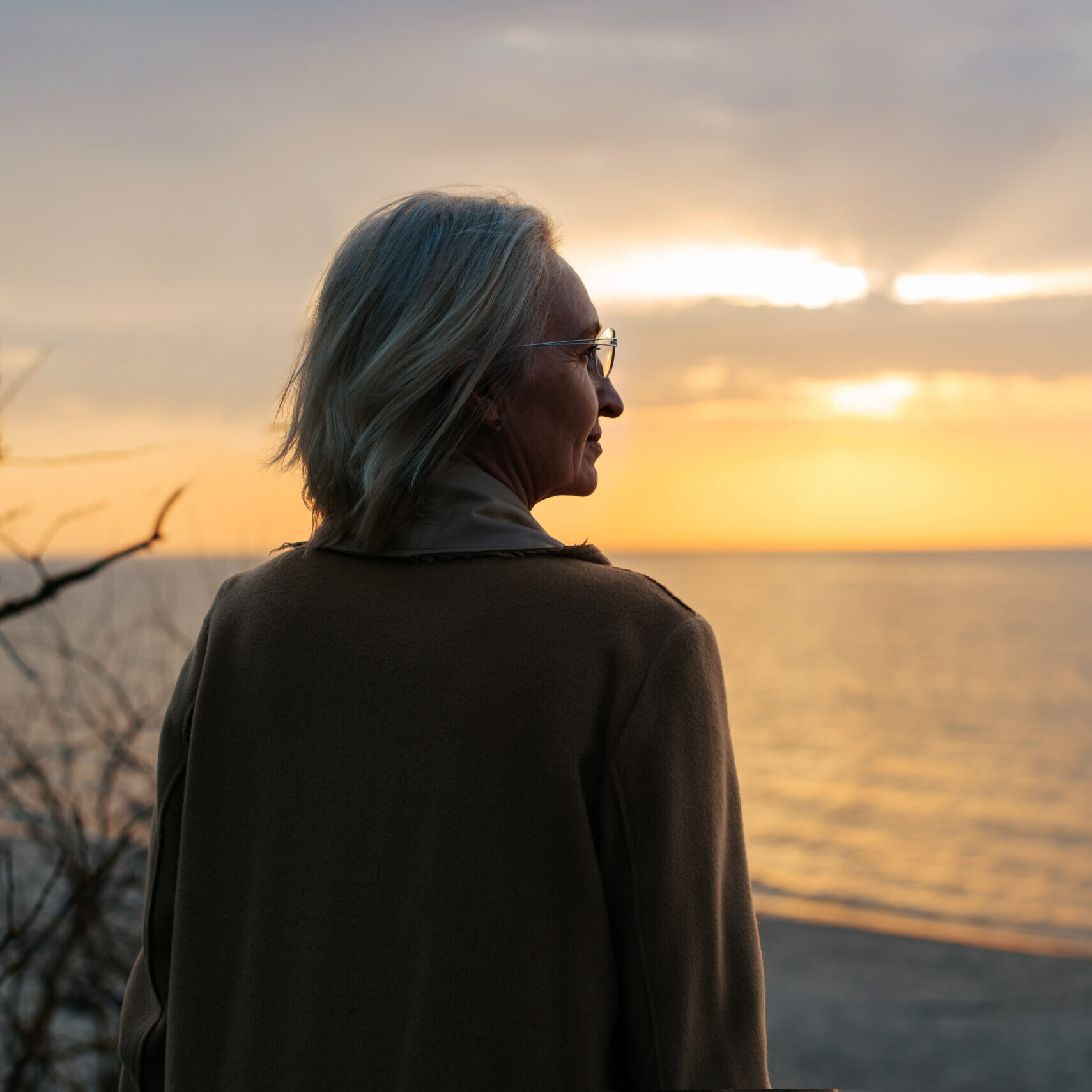 WW Weekend Reflection A woman standing alone at the shore at sunset, looking out across the water